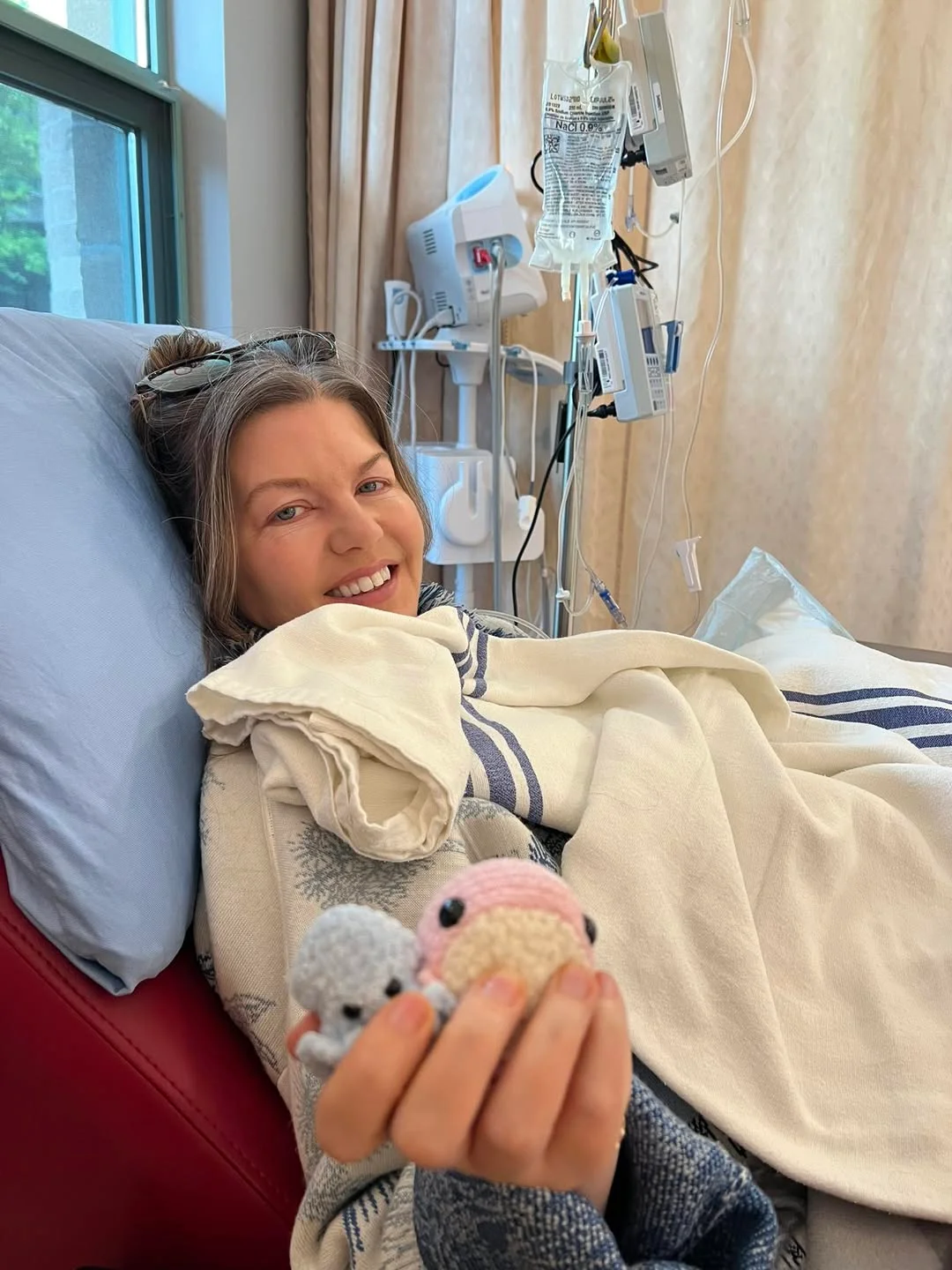Carly in hospital holding two small crocheted creatures, smiling
